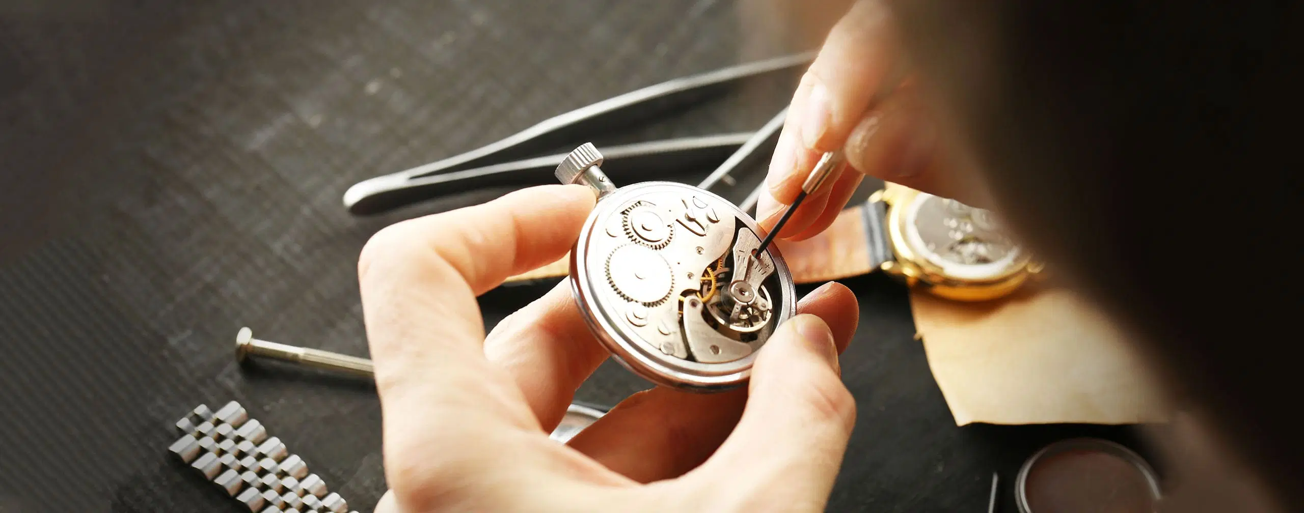 Watchmaker examining a wristwatch beside precision tools on a repair bench